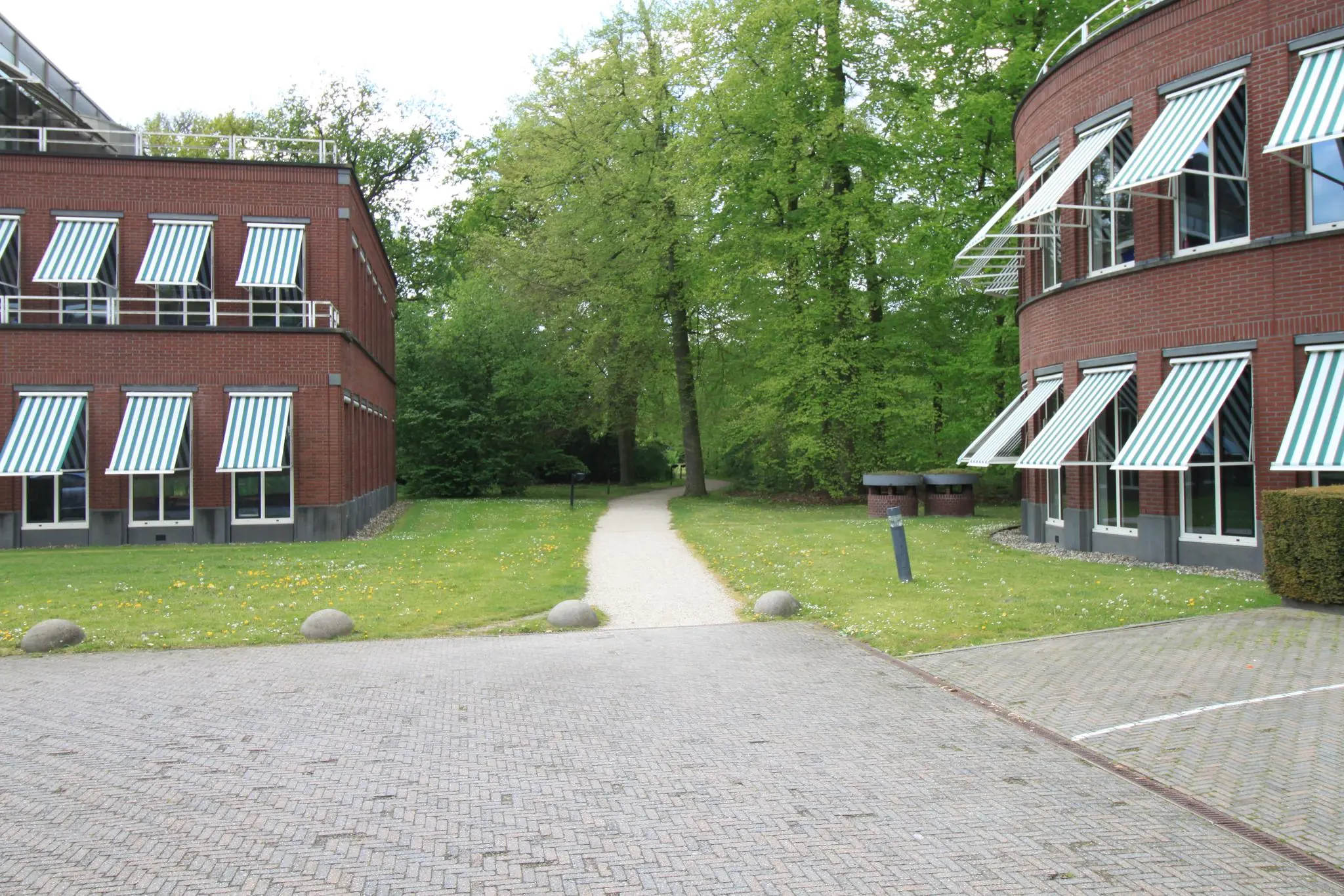 Twee bakstenen kantoorgebouwen aan de Arnhemse Bovenweg met groene zonneschermen en een wandelpad tussen gras en bomen.